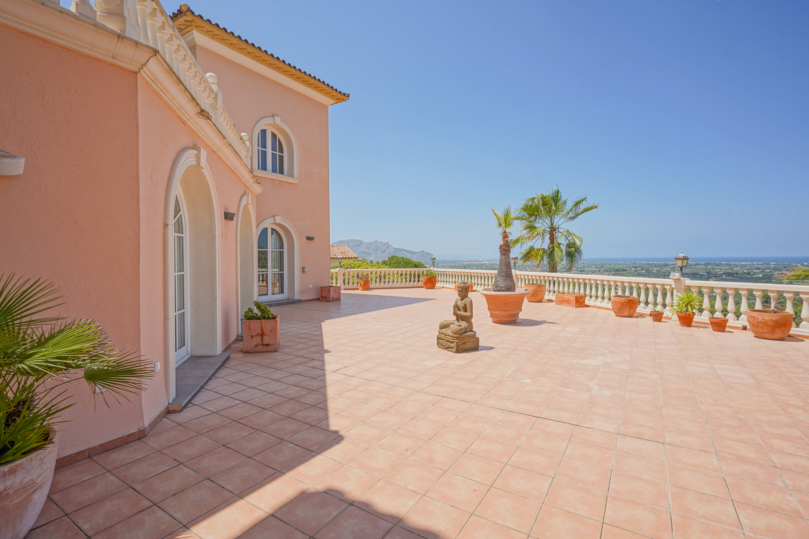 Riant terras met terracotta tegels en een klassieke balustrade met panoramisch zeezicht. De gevel is voorzien van boogvensters en gedecoreerd met mediterrane plantenpotten.