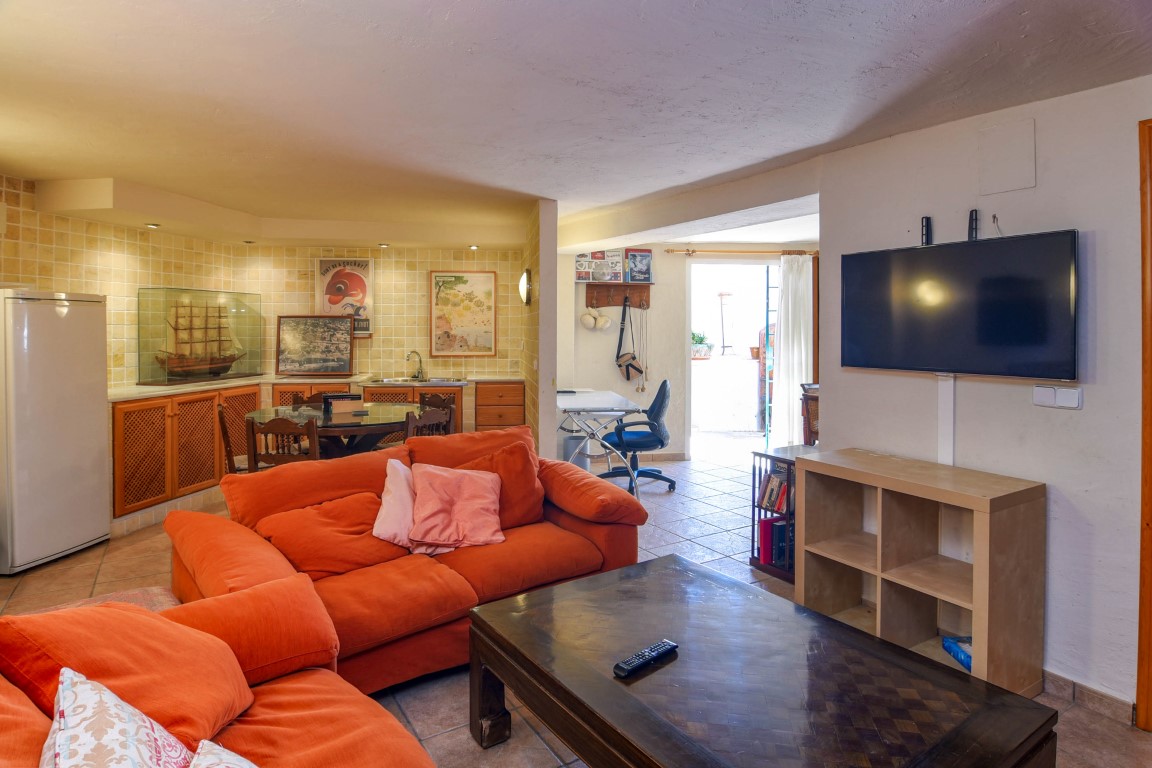 Veelzijdige woonkamer met oranje banken, een bureauhoek en een geïntegreerde kitchenette met houten kasten en rustieke tegels.