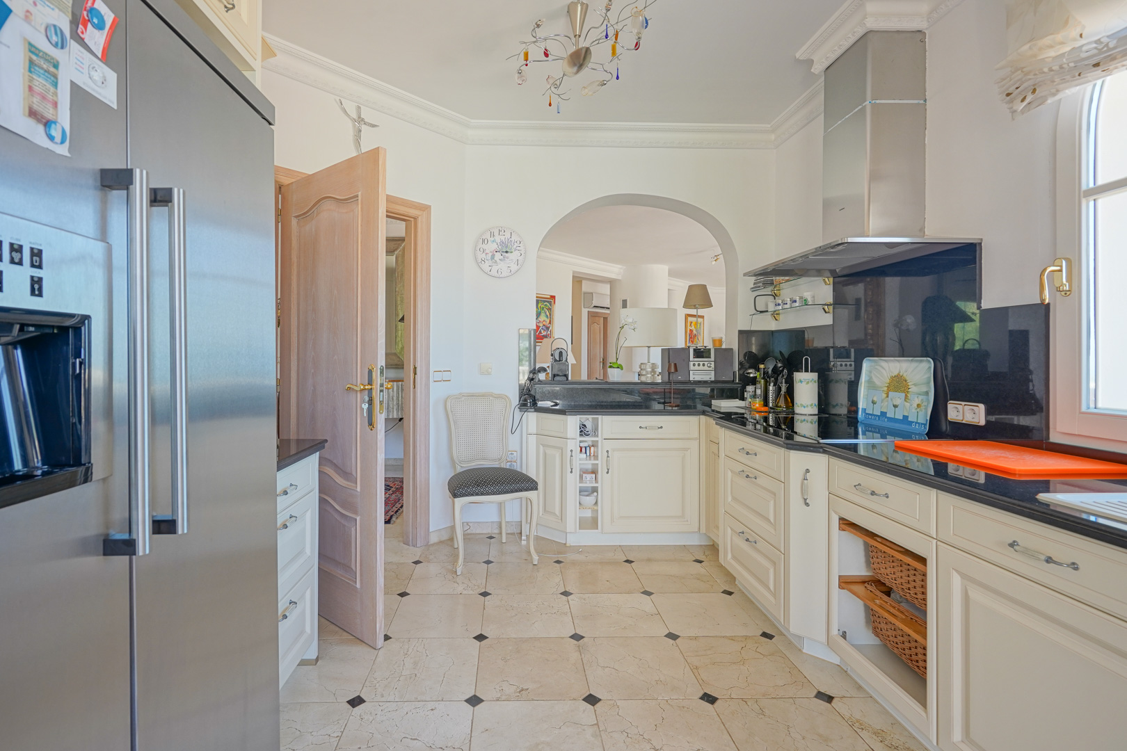 Volledig uitgeruste keuken met crèmekleurige kasten, zwart granieten werkbladen en een marmeren vloer. Voorzien van rvs-apparatuur en een boogverbinding naar de woonkamer.