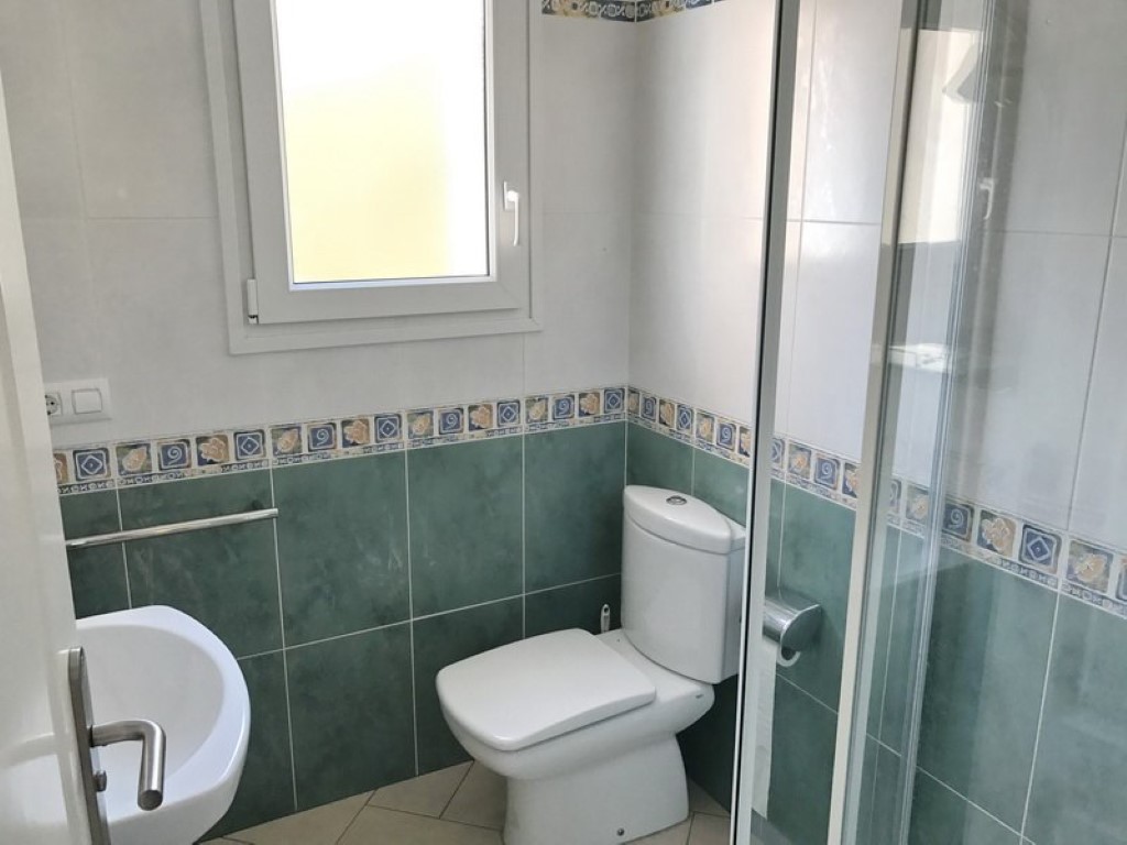 Badkamer met wit sanitair, groen-witte wandtegels met decoratieve rand en een glazen douchecabine voorzien van natuurlijk licht via het raam.