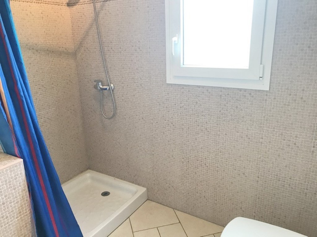 Doucheruimte met beige mozaïektegels, een witte douchebak en een raam met melkglas voor natuurlijke lichtinval en privacy.