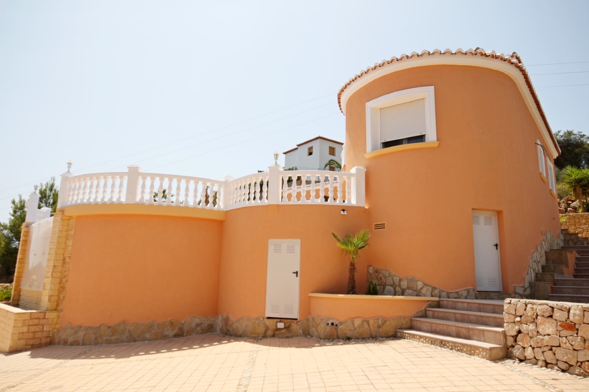 Exterieur van een mediterrane villa met een terracotta ronde toren, witte balustrades en een betegeld terras met natuurstenen details.