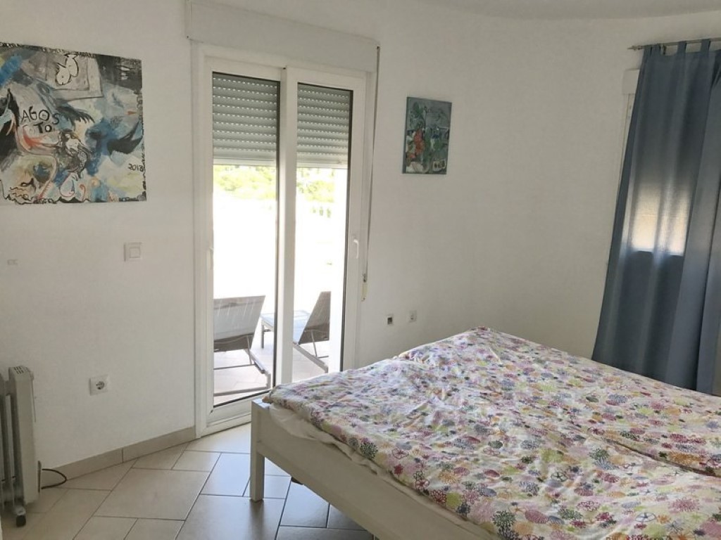 Lichte slaapkamer met een tegelvloer en een schuifpui die direct toegang biedt tot het terras met buitenmeubilair en zonwering.