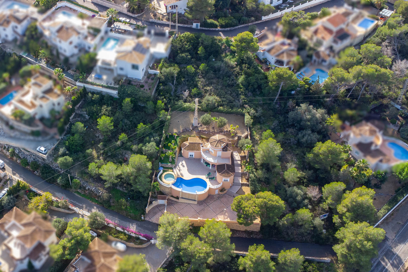 Luchtfoto van de mediterrane villa met een niervormig zwembad, ronde jacuzzi en uitgestrekte geplaveide terrassen, gelegen in een bosrijke omgeving.