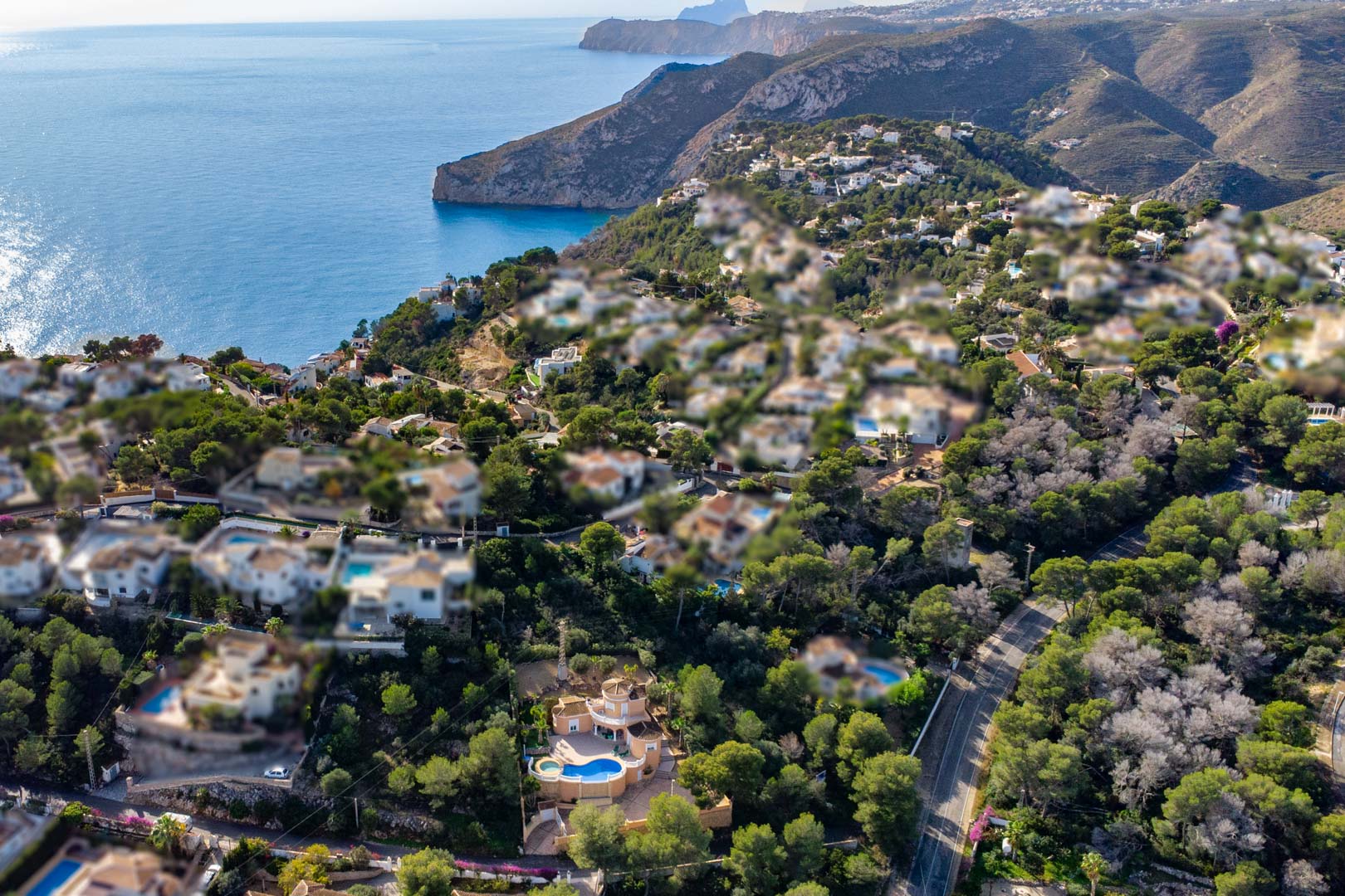Luchtfoto van de villa met een gebogen zwembad en jacuzzi, gelegen tussen de pijnbomen met een panoramisch uitzicht over de Middellandse Zee en de kust van Javea.