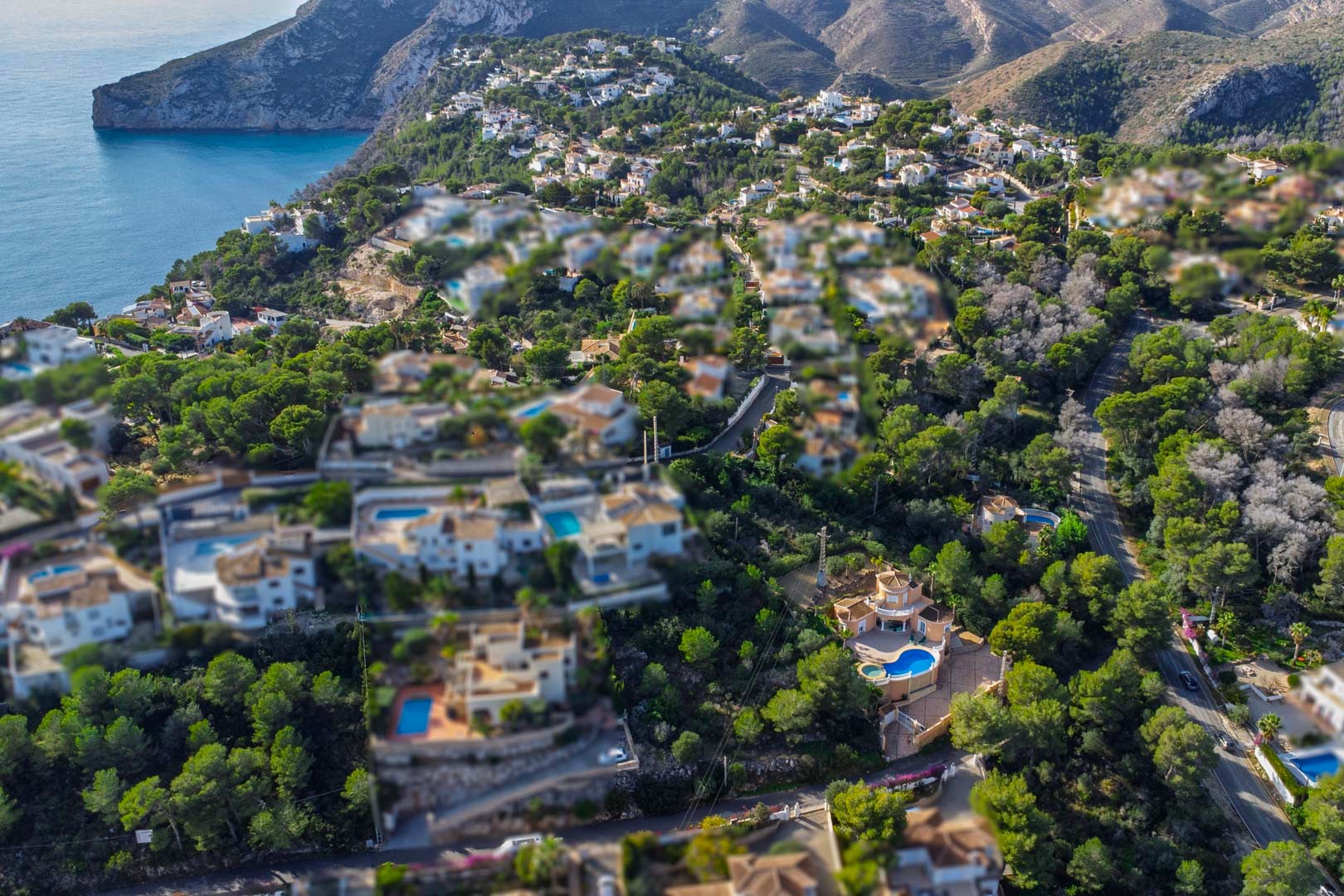 Luchtfoto van een woonwijk in Javea, met mediterrane villa's en privézwembaden gelegen tussen dichte dennenbossen nabij de kustlijn en kliffen.