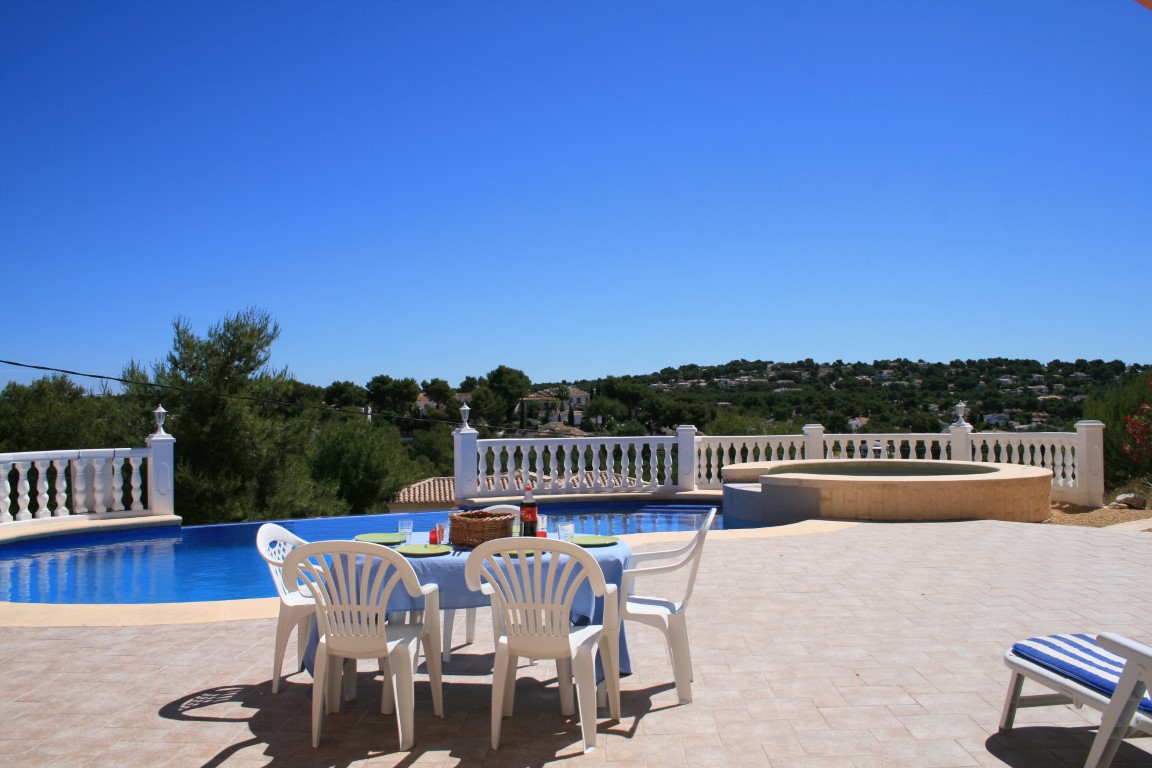 Ruim buitenterras met een niervormig zwembad, geïntegreerde ronde jacuzzi en een eethoek met panoramisch uitzicht over de heuvels van Javea.