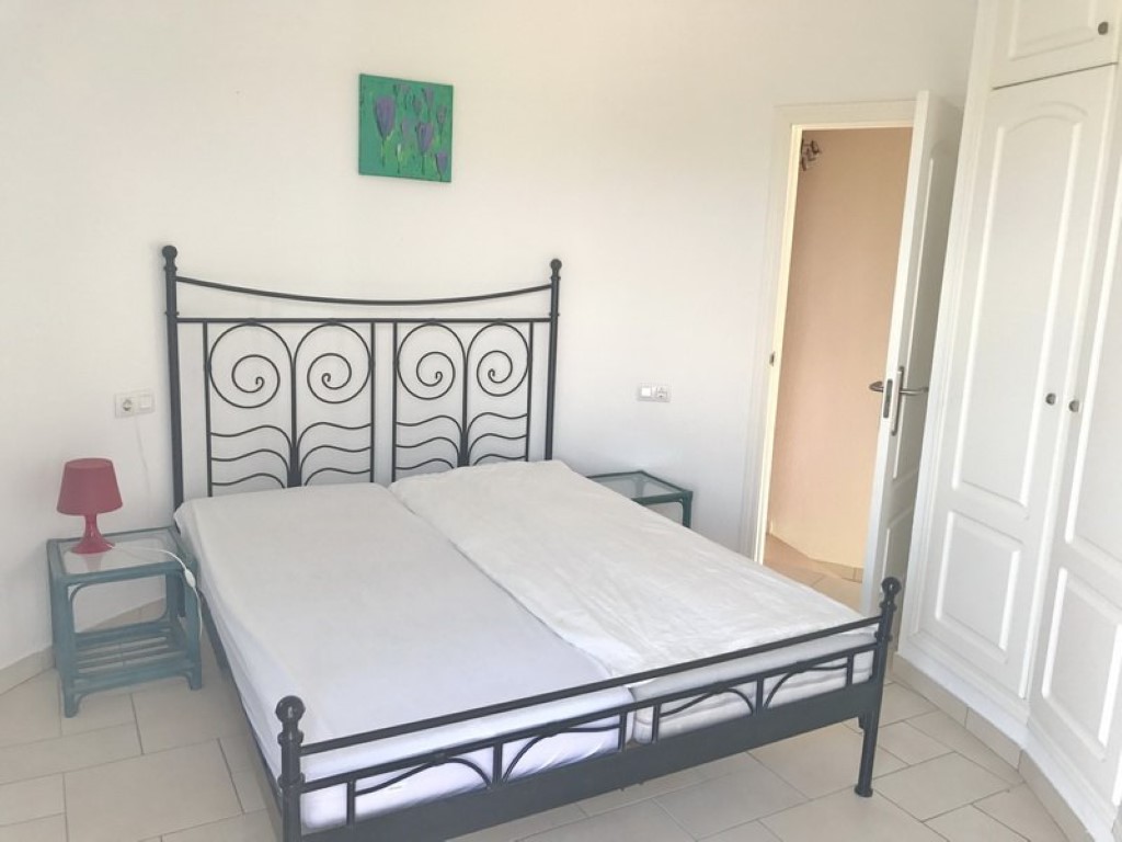 Slaapkamer met een zwart smeedijzeren bedframe, witte inbouwkasten en een lichte tegelvloer. Voorzien van glazen nachtkastjes en een praktische, lichte indeling.