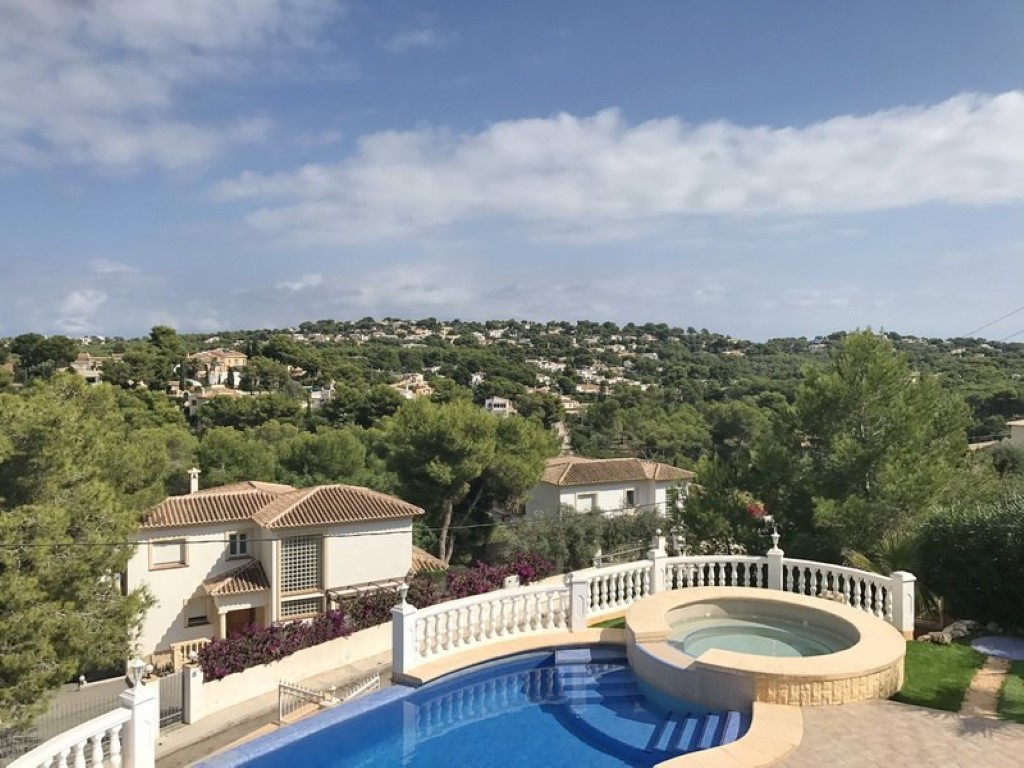 Verhoogd terras met blauw betegeld zwembad en ronde jacuzzi, met panoramisch uitzicht over de met pijnbomen begroeide heuvels en villa's van Javea.
