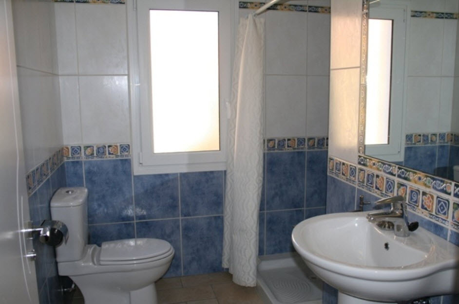 Badkamer met blauw-witte betegeling, een kolomwastafel, douchebak met gordijn en een raam met melkglas voor natuurlijke lichtinval.