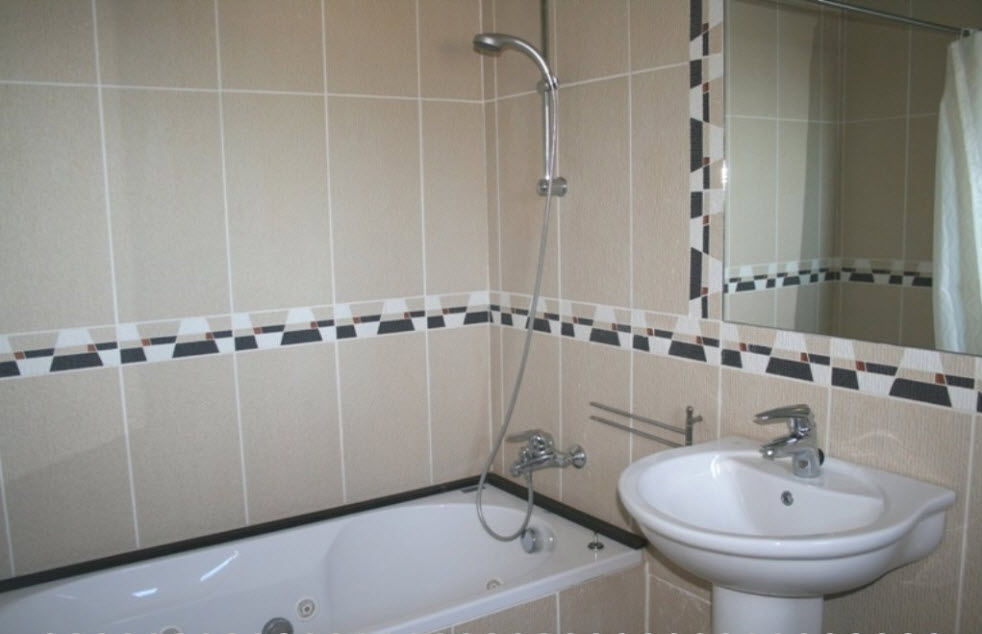 Badkamer voorzien van een hydromassagebad, kolomwastafel en beige wandtegels met een decoratieve geometrische rand.
