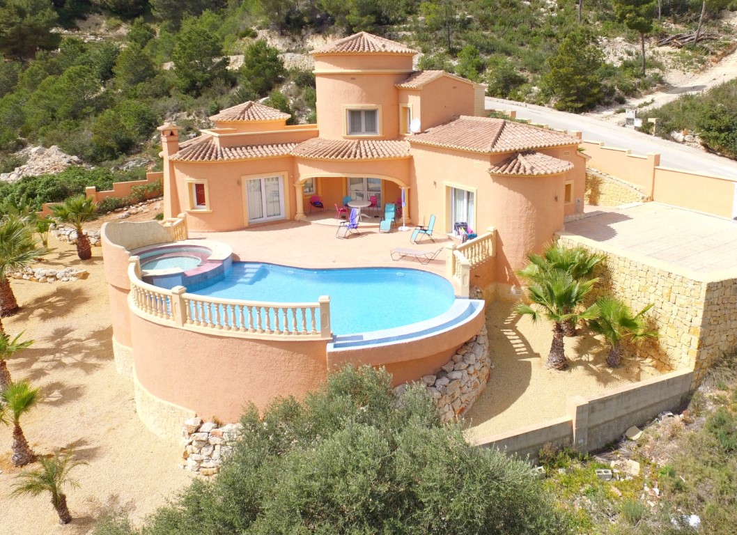 Exterieur van de mediterrane villa met een gebogen overloopzwembad, geïntegreerde jacuzzi en zonneterras omgeven door palmbomen.