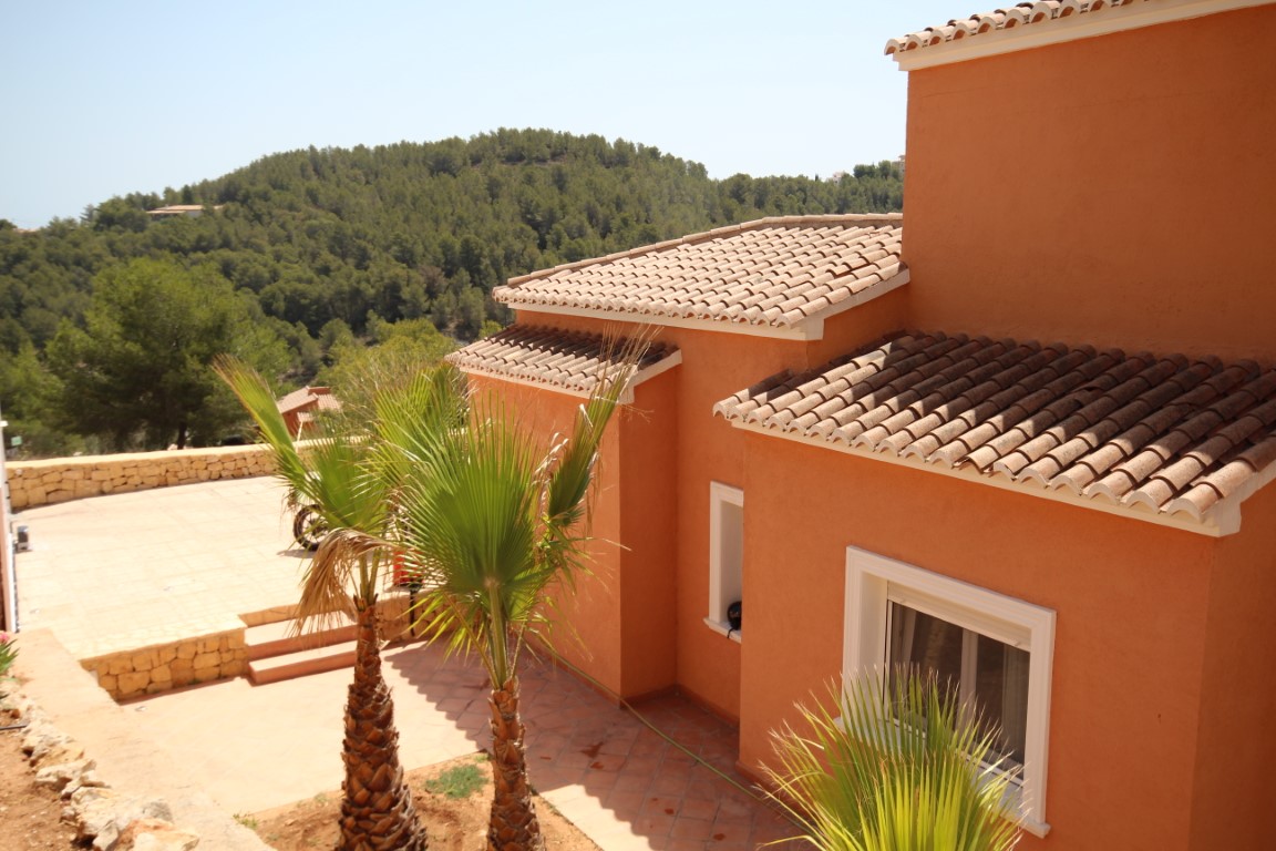 Mediterrane gevel in terracottakleuren met traditionele pannendaken, een betegeld terras met palmbomen en uitzicht op de omliggende groene heuvels.