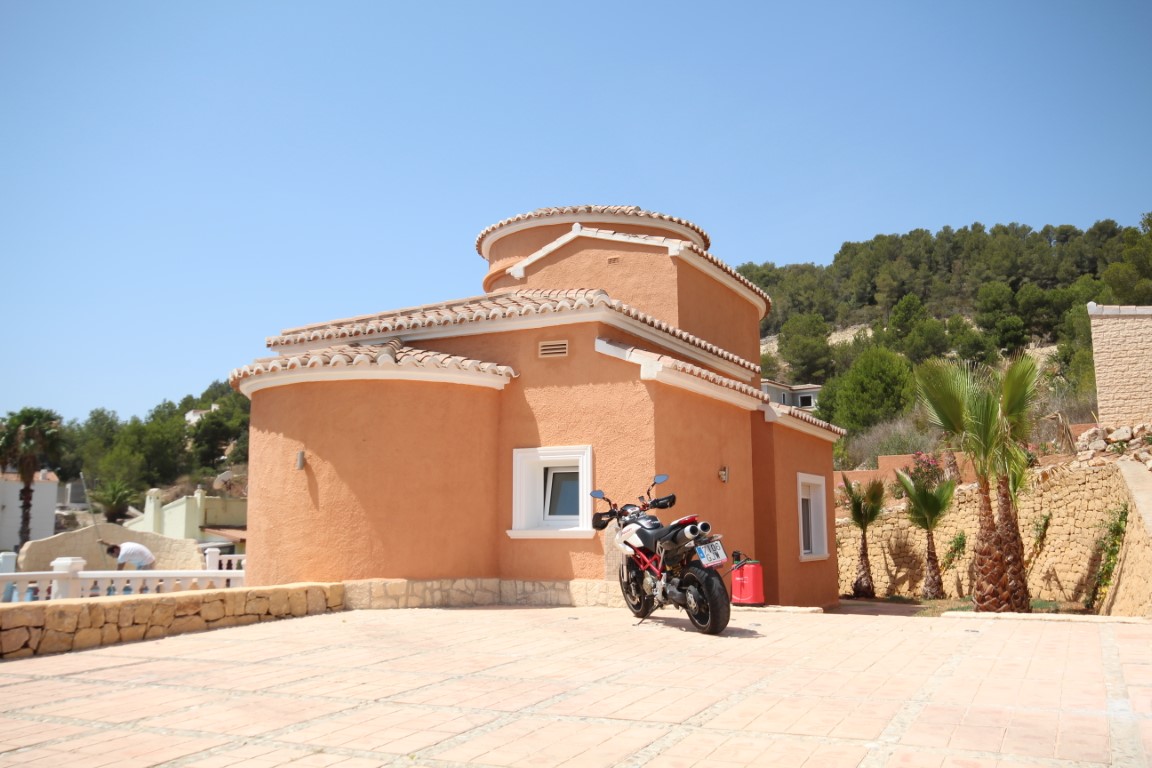 Mediterrane gevel met ronde terracotta muren, een ruime geplaveide parkeerplaats en natuurstenen muren met jonge palmbomen.