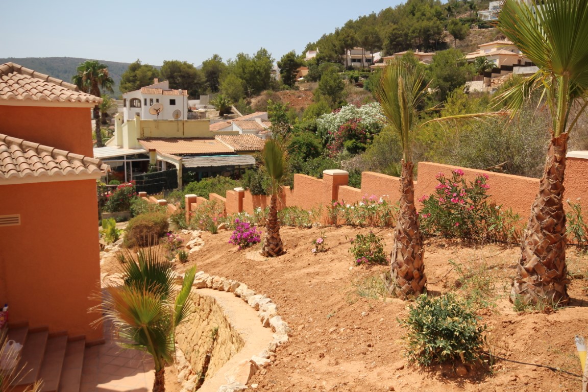 Mediterrane terrastuin met jonge palmbomen, bloeiende struiken en terracotta muren die uitkijken over de omliggende heuvelachtige woonwijk.