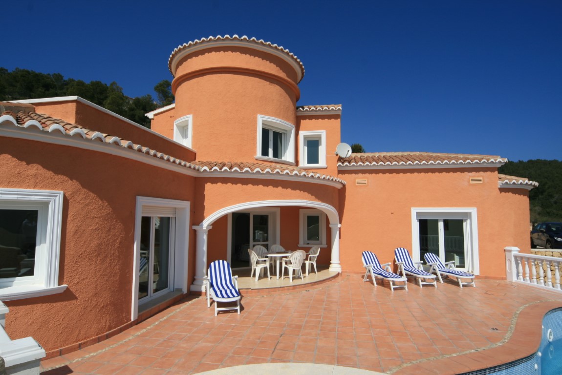 Mediterrane villa met terracotta gevel, ronde toren en een ruim betegeld zonneterras met gestreepte ligstoelen en een overdekte naya bij het zwembad.