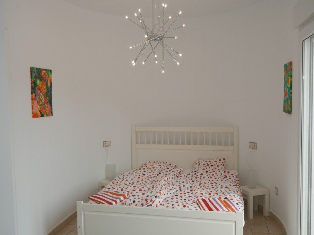 Slaapkamer met wit houten bed, een moderne designlamp en directe toegang naar buiten via een glazen schuifdeur.