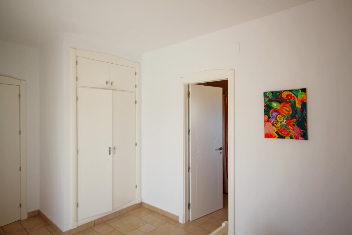 Slaapkamer met witte inbouwkast, terracotta vloertegels en witte wanden voorzien van een kleurrijk abstract kunstwerk.