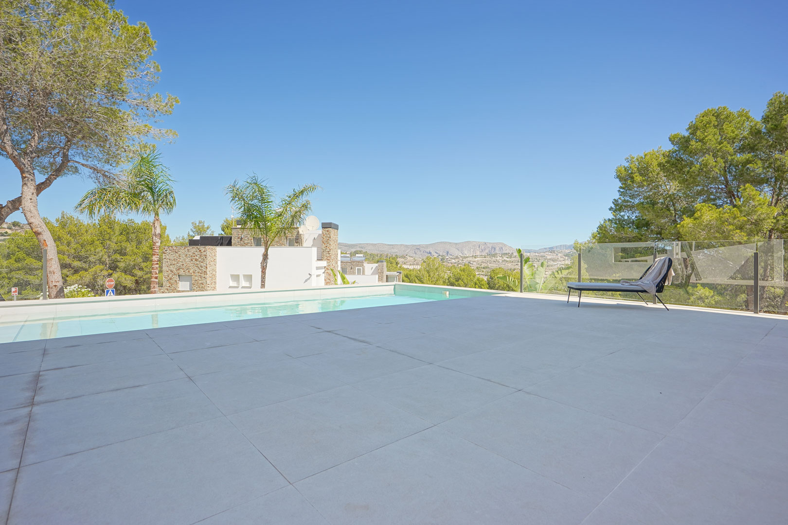 Ruim terras met grootformaat tegels, een overloopzwembad en glazen balustrade met panoramisch uitzicht over de vallei en de pijnbomen.