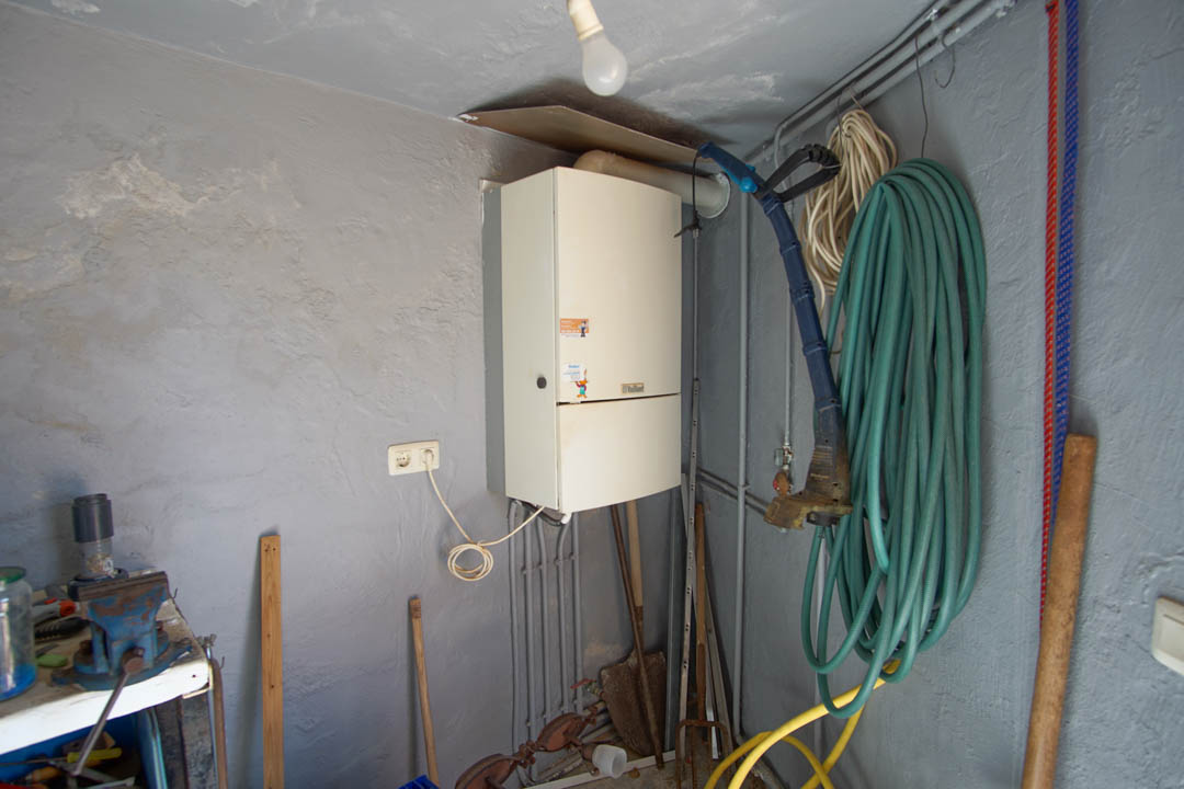 Functionele technische ruimte en berging met een wandgemonteerde cv-ketel, werkbank met bankschroef en opbergruimte voor tuingereedschap.