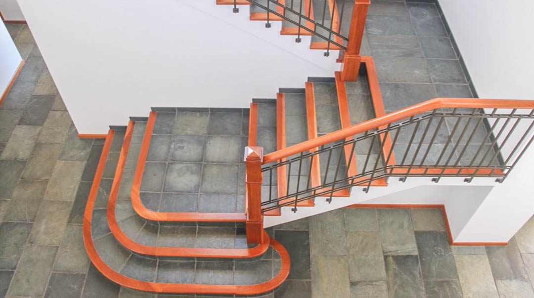 Centrale trap met natuurstenen treden en hardhouten afwerking. De smeedijzeren leuning met houten handgreep vormt een elegant contrast met de donkere tegelvloer.