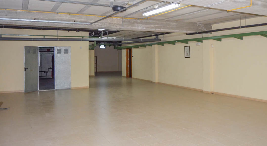 Ruime ondergrondse garage voorzien van tegelvloer, zichtbare betonnen plafondbalken en technische ruimtes met metalen deuren.