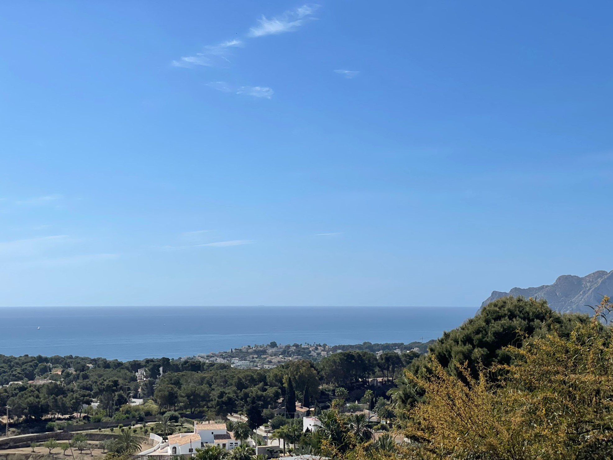 Panoramisch uitzicht op de kustlijn van Benissa, met mediterrane vegetatie, residentiële villa's en de zee onder een helderblauwe lucht.