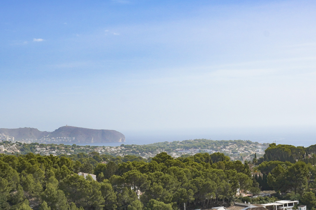 Verhoogd panoramisch uitzicht op de Cap D'or in Moraira, met dichte mediterrane pijnbomen en de kustlijn onder een heldere hemel.