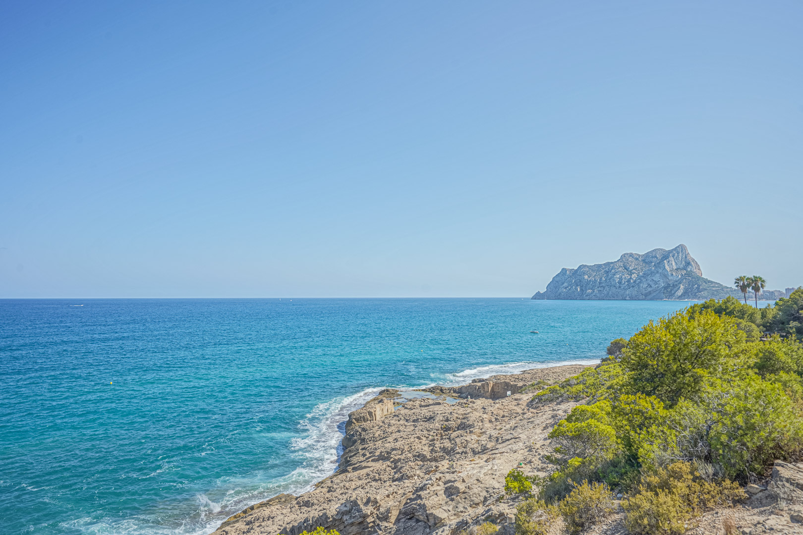 Panoramisch uitzicht op de rotsachtige kustlijn van Benissa met de Peñón de Ifach in de verte en het heldere turquoise water van de Middellandse Zee.