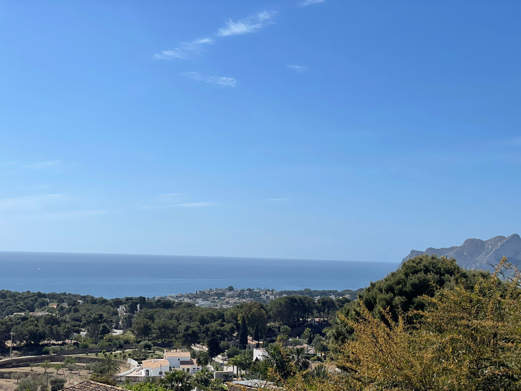 Panoramisch uitzicht vanaf het perceel over de kustlijn van Benissa, met dichte mediterrane begroeiing en de zee onder een helderblauwe lucht.