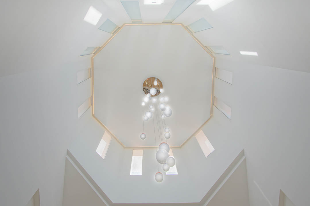 Bovenaanzicht van het achthoekige plafond met symmetrische dakramen en een moderne glazen bolkroonluchter in het dubbelhoge trappenhuis.