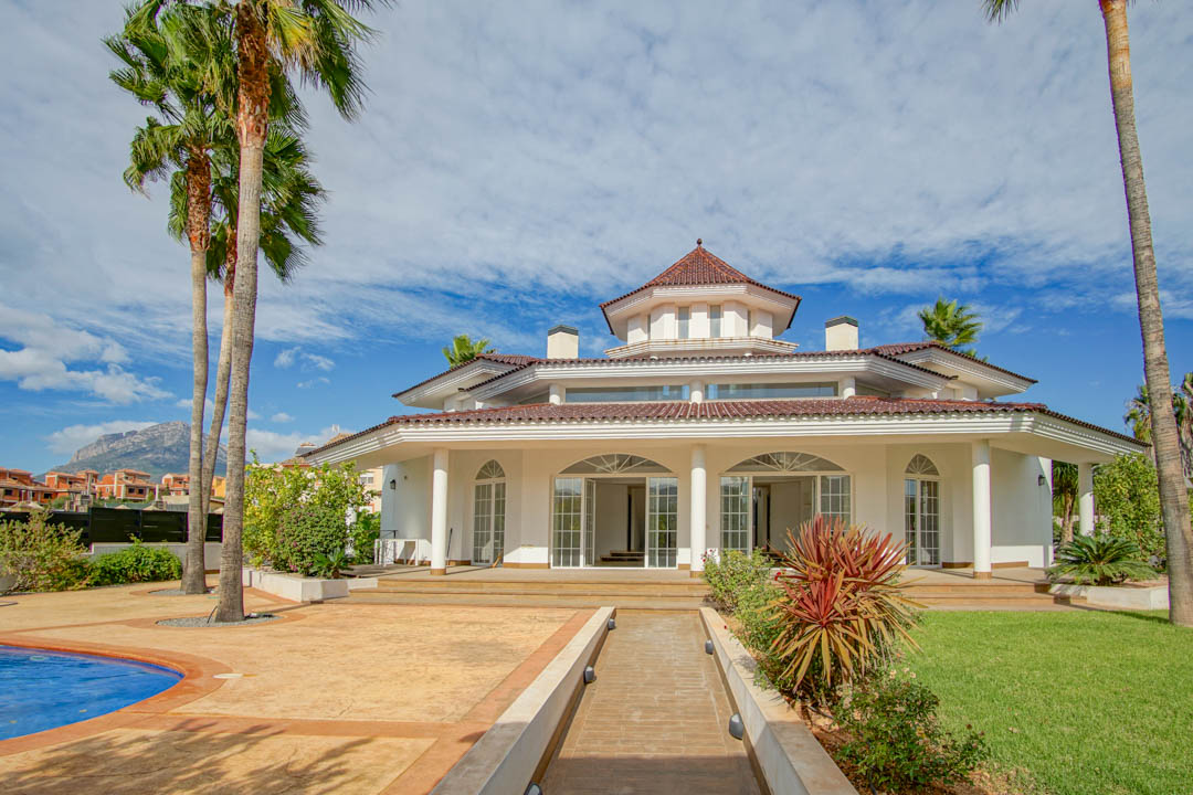 Exterieur van een koloniale villa met witte gevel, zuilengalerij, centrale achthoekige toren en tuin met palmbomen en zwembad.
