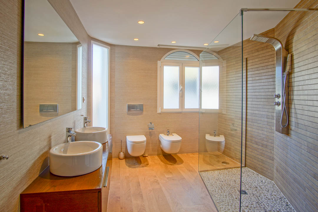 Moderne badkamer met dubbele wastafel op houten meubel, inloopdouche met kiezelvloer en hangend sanitair met subtiele inbouwverlichting.
