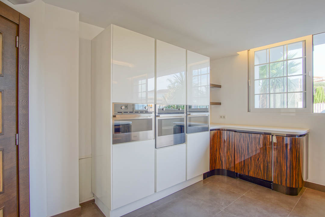Moderne keuken met witte hoogglanskasten, geïntegreerde roestvrijstalen ovens en gebogen onderkasten met een opvallende donkere houtnerf afwerking.