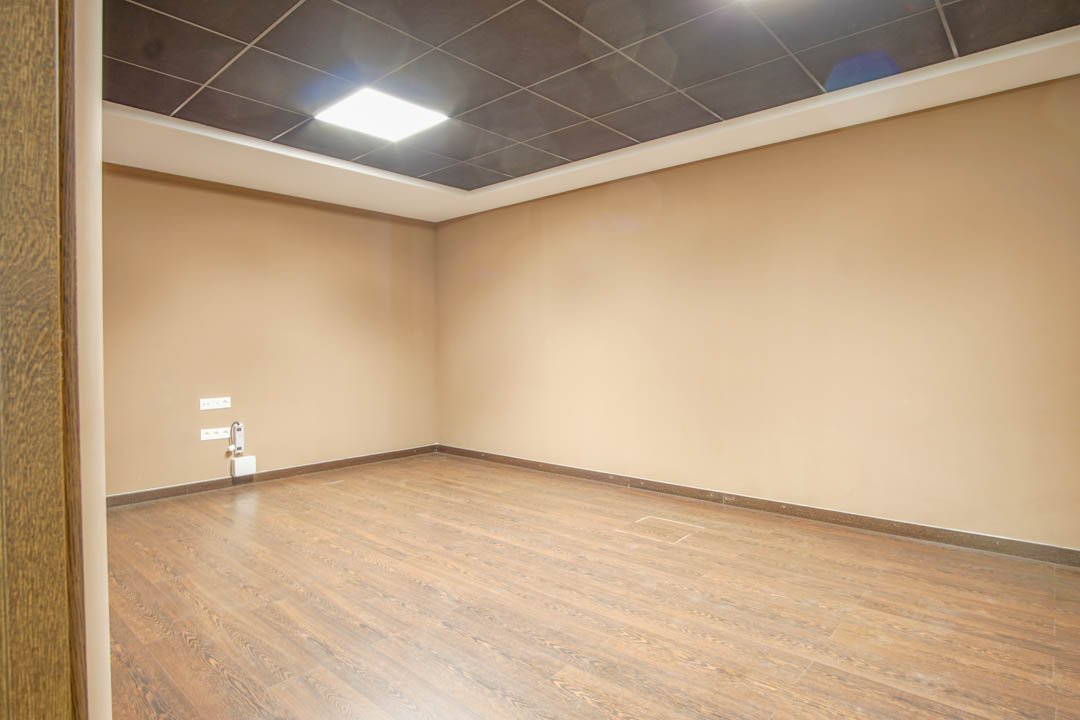 Multifunctionele ruimte in het souterrain met houtlook vloer, beige wanden en een systeemplafond met geïntegreerde LED-verlichting.