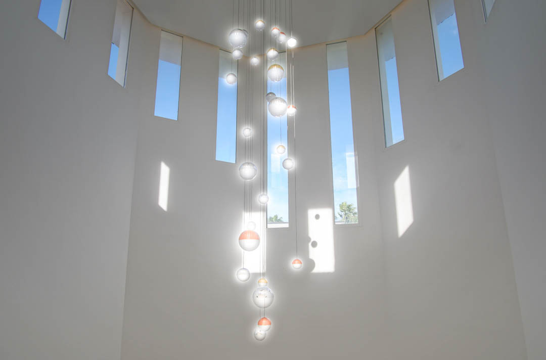 Plafond met dubbele hoogte voorzien van een moderne glazen bolkroonluchter en smalle verticale ramen die zorgen voor een overvloed aan natuurlijk licht.