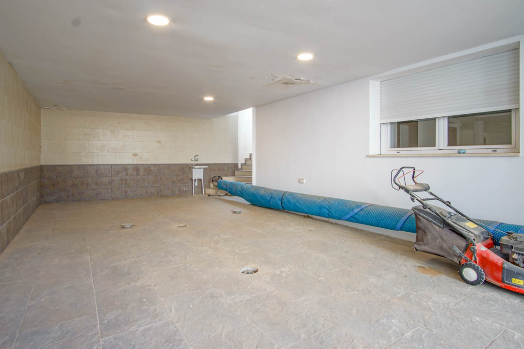 Ruime garage voorzien van keramische tegelvloer, inbouwspots en een praktische gootsteen. De ruimte biedt directe toegang tot de woning en opslag voor tuinmachines.