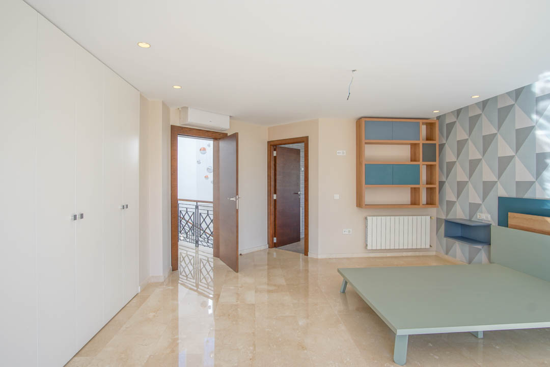 Slaapkamer met gepolijste marmeren vloer, kamerhoge witte inbouwkasten en een geometrische accentmuur. Voorzien van een houten wandmeubel en toegang tot de overloop.