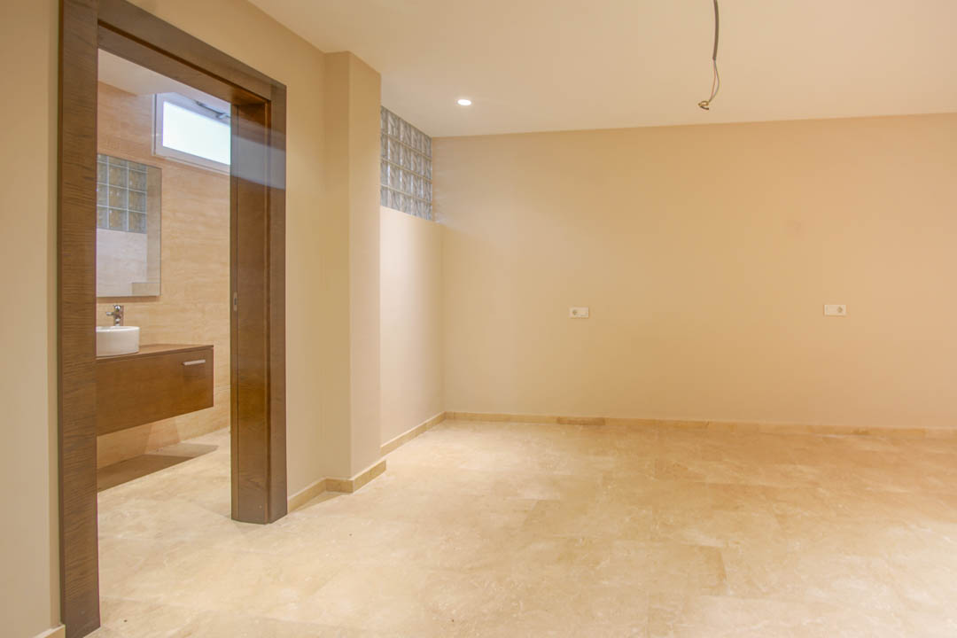 Slaapkamer met natuurstenen vloer en aangrenzende badkamer. Voorzien van een zwevend houten wastafelmeubel, glazen bouwstenen en neutrale wandafwerking.