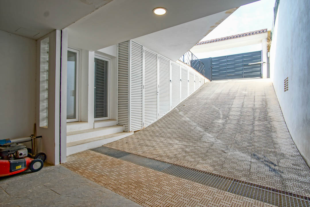 Toegangshelling naar de garage met antislipvloer, witte lamellen opbergkasten en een secundaire ingang met glazen deuren.