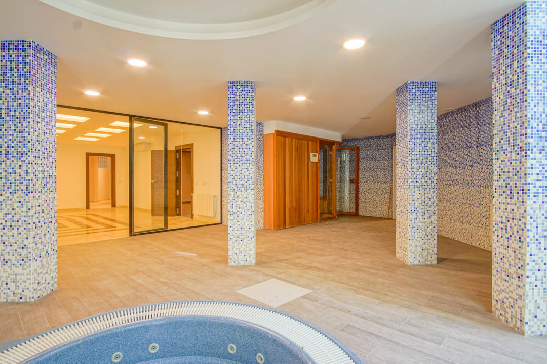 Wellnessruimte met rond bubbelbad, houten sauna en blauwe mozaïekzuilen. Voorzien van inbouwspots en glazen wanden die uitkijken op de rest van het souterrain.