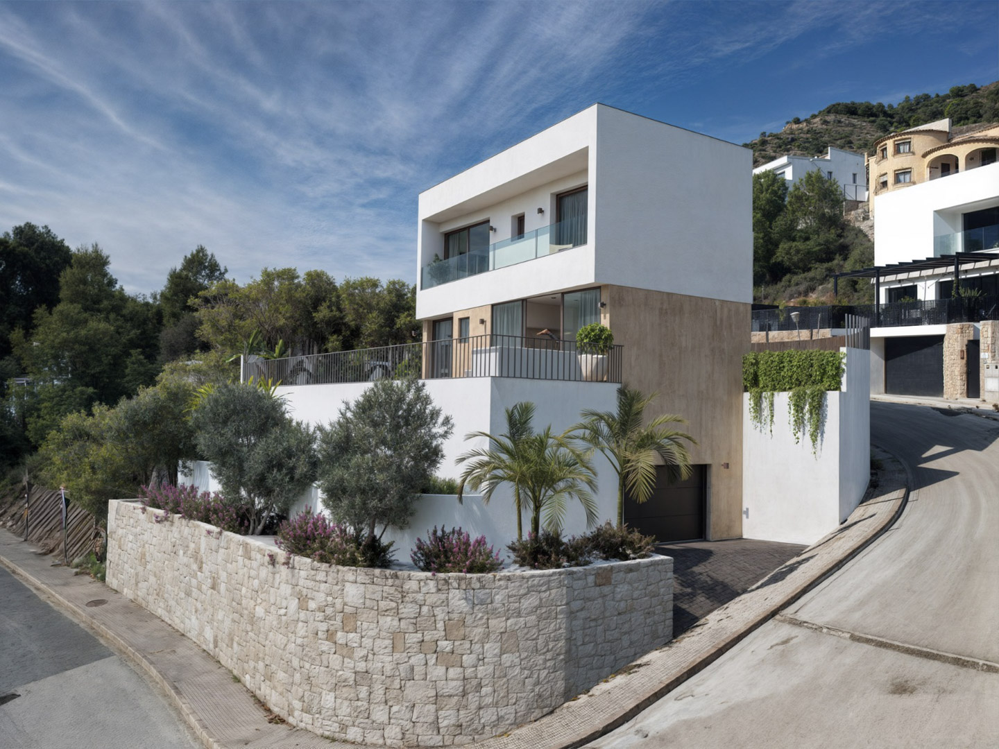 Moderne villa met drie verdiepingen, natuurstenen gevel, terrassen met glazen balustrades en een in het souterrain geïntegreerde garage.
