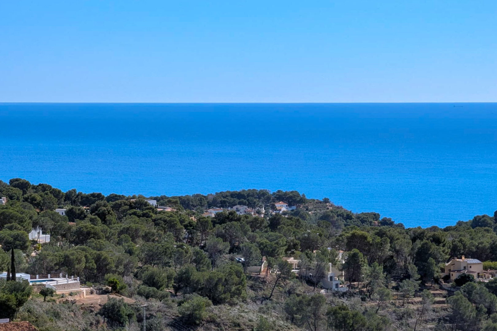 Panoramisch uitzicht vanaf het perceel over de Middellandse Zee en de met pijnbomen begroeide heuvels van Benissa tegen een heldere horizon.