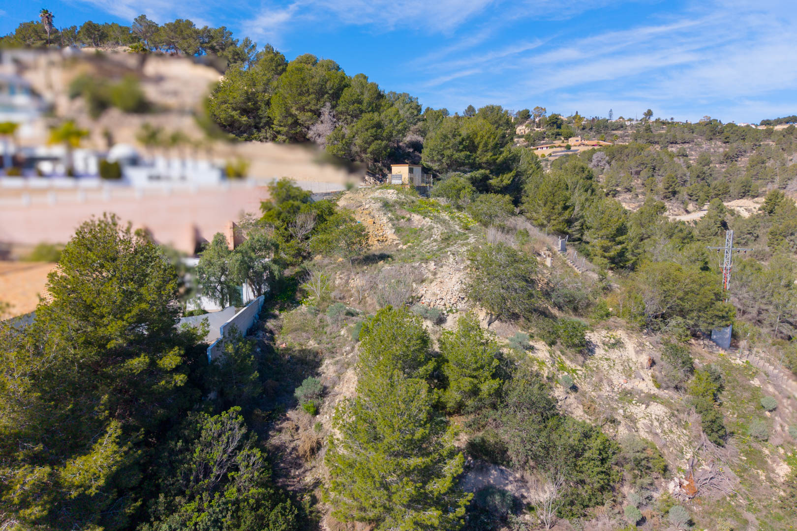 Steil perceel in Tossal Los Bancales met mediterrane pijnbomen, natuurlijke begroeiing en aanwezige nutsvoorzieningen op een helling.