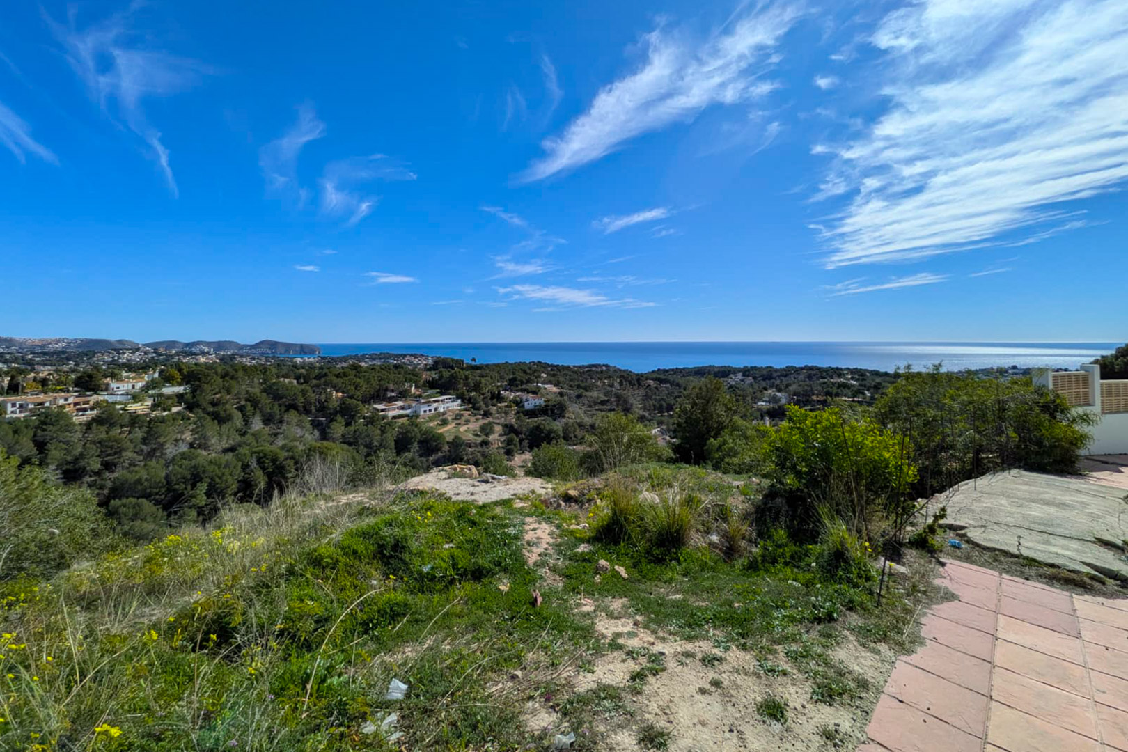 Verhoogd panoramisch uitzicht vanaf het perceel over de Middellandse Zee, Cap D'or en de groene heuvels van Benissa bij een heldere hemel.