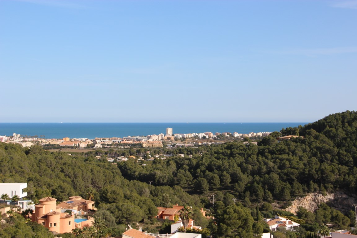 Panoramisch uitzicht op de Middellandse Zee en de kustlijn van Jávea vanaf de hooggelegen percelen, omgeven door een dicht dennenbos.