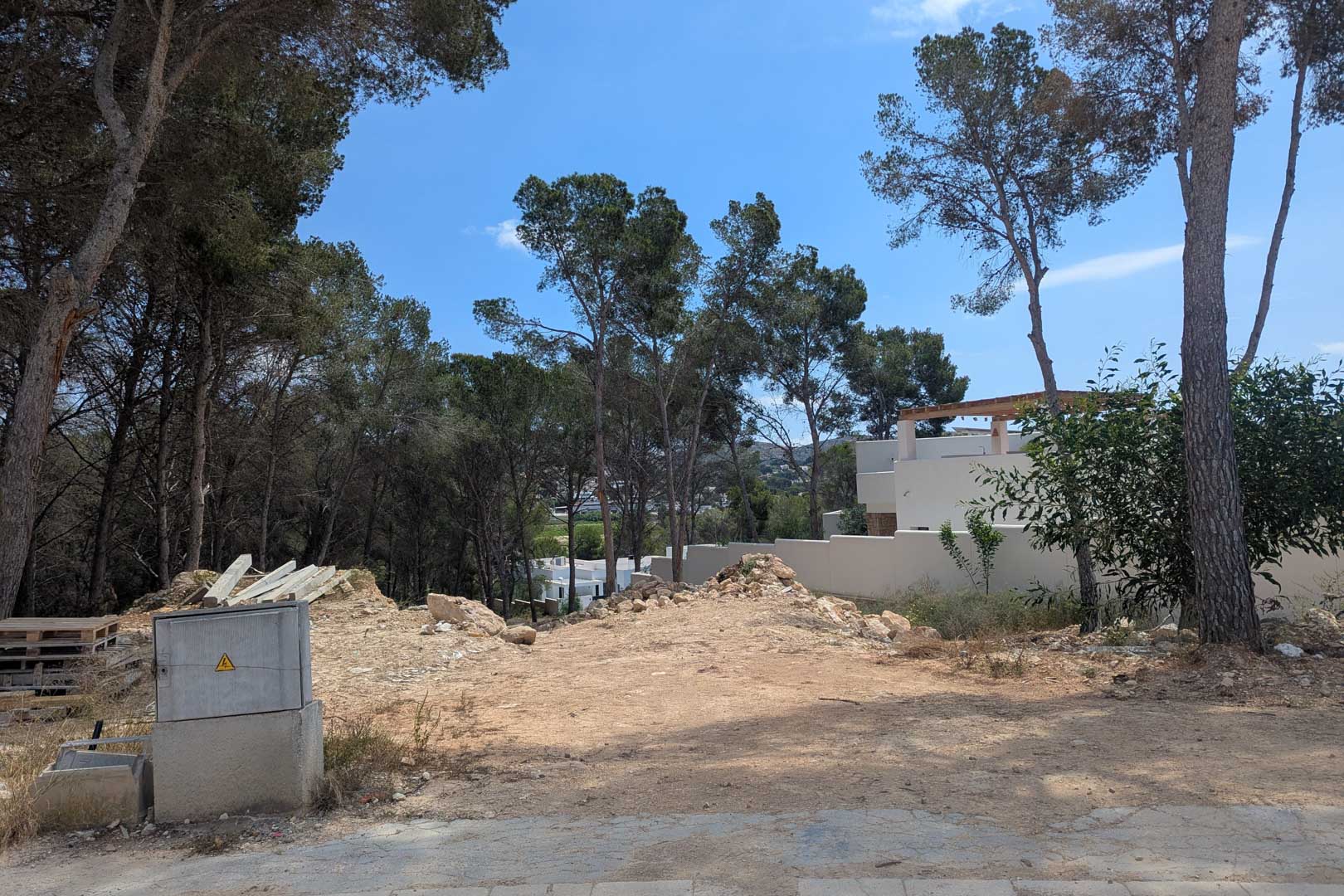 Hooggelegen bouwperceel omgeven door volwassen pijnbomen in Moraira, met bouwrijpe grond en aansluitingen klaar voor de directe start van de bouw.