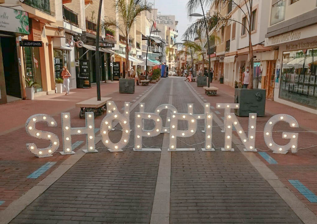 Voetgangersvriendelijke winkelstraat in het centrum van Moraira met palmbomen, boetieks en een grote verlichte decoratie op de voorgrond.