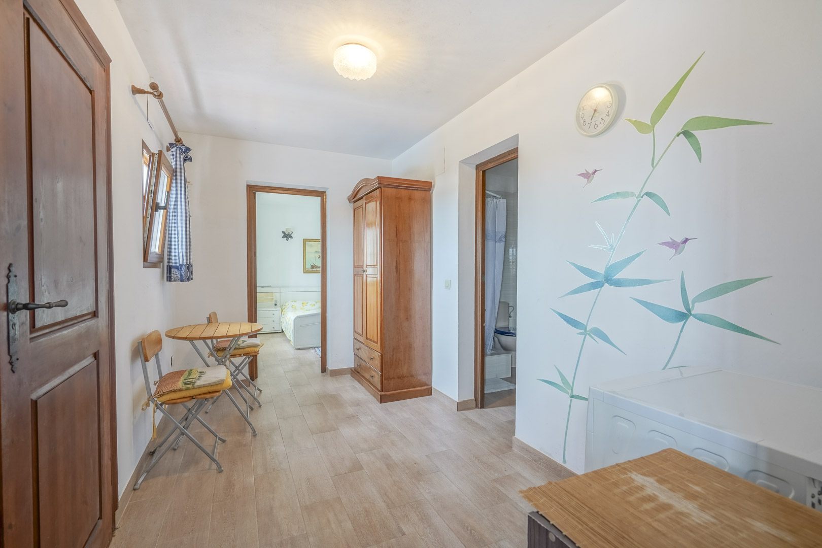 Licht interieur met tegelvloeren, een houten kledingkast en botanische wanddecoratie.
