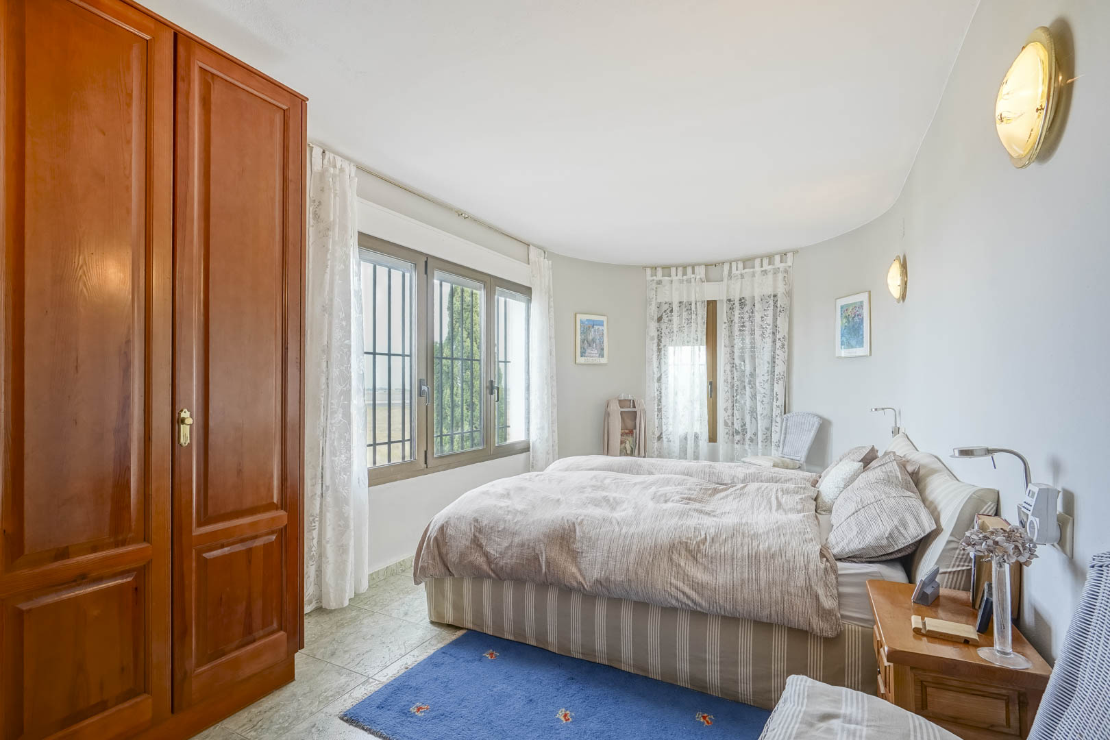 Lichte slaapkamer met houten kledingkast, ramen met uitzicht en gestreept beddengoed.